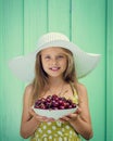 Beautiful blond girl on a background of turquoise wall in the white hat holding plate with cherry. Royalty Free Stock Photo