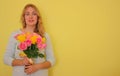 Beautiful blond girl in the blue dress holding bouquet of yellow and pink roses on a light-yellow background. Royalty Free Stock Photo