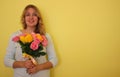 Beautiful blond girl in the blue dress holding bouquet of yellow and pink roses on a light-yellow background. Royalty Free Stock Photo