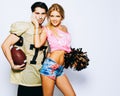 Beautiful blond girl cheerleader with PP Duster and a quarterback player american football posing with a ball. Super