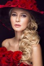 Beautiful blond girl in dress and hat with roses, classic makeup, curls, red lips. Beauty face. Royalty Free Stock Photo