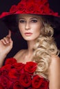 Beautiful blond girl in dress and hat with roses, classic makeup, curls, red lips. Beauty face. Royalty Free Stock Photo