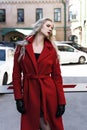 A beautiful blond girl wearing a red coat and gloves stands near the barrier among old buildings. Fashionable, industrial, Royalty Free Stock Photo