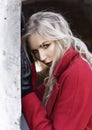 A beautiful blond girl wearing a red coat and gloves stands by a ruined wall and brick arch near an old building. Fashionable, Royalty Free Stock Photo