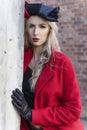 A beautiful blond girl wearing a red coat and gloves stands by a ruined wall and brick arch near an old building. Fashionable, Royalty Free Stock Photo