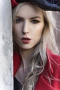 A beautiful blond girl wearing a red coat and gloves stands by a ruined wall and brick arch near an old building. Fashionable, Royalty Free Stock Photo