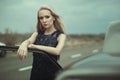 Beautiful blond lady in luxurious dark blue sequin tassel evening dress standing at her old car with open hood Royalty Free Stock Photo