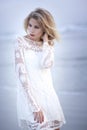 Beautiful blond model on the beach with flowing hair in wind and white lace dress. Royalty Free Stock Photo