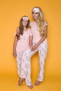 Beautiful blond girls, mother with daughter in pajamas on a yellow background in the studio.