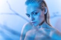 Beautiful blond model with nude make up, slicked back hair and naked shoulders in blue light