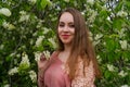 woman in pink outfit is posing in botanical garden park near blooming bird cherry mayday tree with flowers