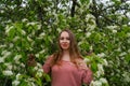 woman in pink outfit is posing in botanical garden park near blooming bird cherry mayday tree with flowers