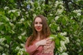 woman in pink outfit is posing in botanical garden park near blooming bird cherry mayday tree with flowers