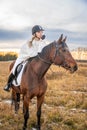 Beautiful blond professional female jockey riding a horse in field. Friendship with horse. Royalty Free Stock Photo