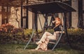 Beautiful Blond Red-haired woman girl model rests in swing boat garden house alcove.