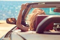 Beautiful blond smiling young woman in convertible top automobile looking sideways while parked near ocean waterfront Royalty Free Stock Photo