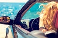 Beautiful blond smiling young woman in convertible top automobile looking sideways while parked near ocean waterfront Royalty Free Stock Photo