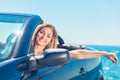 Beautiful blond smiling young woman in convertible top automobile looking sideways while parked near ocean waterfront Royalty Free Stock Photo