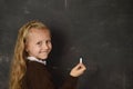 Beautiful blond sweet schoolgirl in uniform holding chalk writing on blackboard smiling happy Royalty Free Stock Photo