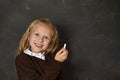 Beautiful blond sweet schoolgirl in uniform holding chalk writing on blackboard smiling happy Royalty Free Stock Photo