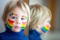 Beautiful blond toddler boy with rainbow painted on his face and messy hands