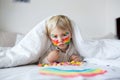 Beautiful blond toddler boy with rainbow painted on his face and messy hands