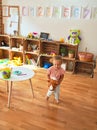 Beautiful blond toddler girl ridding horse with stick toy at kindergarten