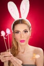 Beautiful blond woman as Easter bunny with rabbit ears on red background, studio shot. Young lady holding three colored eggs Royalty Free Stock Photo