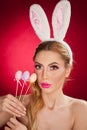 Beautiful blond woman as Easter bunny with rabbit ears on red background, studio shot. Young lady holding three colored eggs Royalty Free Stock Photo