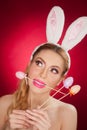 Beautiful blond woman as Easter bunny with rabbit ears on red background, studio shot. Young lady holding three colored eggs Royalty Free Stock Photo