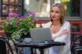 Beautiful blond woman dressed in  light clothes sitting in outdoor cafe and working with computer - image Royalty Free Stock Photo