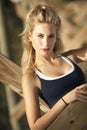 A beautiful blond woman with her hair in a pony tail sitting under pier near ocean. Royalty Free Stock Photo