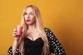 Beautiful blond woman holds paper red cup with juice isolated on yellow background. Royalty Free Stock Photo