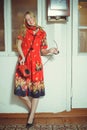 Beautiful blond woman with an old wired phone dressed in a red dress, standing in an old house, vintage style Royalty Free Stock Photo