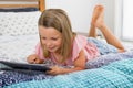 Beautiful blond 6 or 7 years old young girl lying on bed smiling happy using the internet on digital tablet pad watching and havin Royalty Free Stock Photo