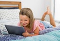 Beautiful blond 6 or 7 years old young girl lying on bed smiling happy using the internet on digital tablet pad watching and havin Royalty Free Stock Photo