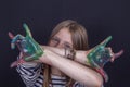 Beautiful blond young girl with freckles and hands painted in colorful paints indoors on black background, closeup portrait Royalty Free Stock Photo