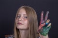 Beautiful blond young girl with freckles and hands painted in colorful paints indoors on black background, closeup portrait Royalty Free Stock Photo