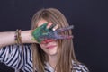 Beautiful blond young girl with freckles and hands painted in colorful paints indoors on black background, closeup portrait Royalty Free Stock Photo