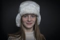 Beautiful blond young girl with a winter fur hat indoors on a black background, closeup portrait Royalty Free Stock Photo