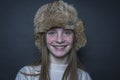 Beautiful blond young girl with a winter fur hat indoors on a black background, closeup portrait Royalty Free Stock Photo