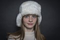 Beautiful blond young girl with a winter fur hat indoors on a black background, closeup portrait Royalty Free Stock Photo