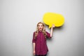 Beautiful blond young woman holding yellow blank speech bubble over grey background Royalty Free Stock Photo