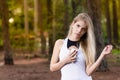 Beautiful blond young woman in park at sunset holding mobile near chest - Image