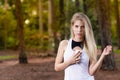 Beautiful blond young woman in park at sunset holding mobile near chest - Image