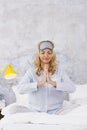 Beautiful blond and young woman, wearing sleeping mask, sitting in bed and doing yoga exercises in the morning Royalty Free Stock Photo