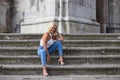 Beautiful blonde adult woman dressed in jeans and white top sitting on the steps of the cathedral in Cadiz, Spain. The woman is Royalty Free Stock Photo