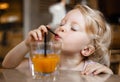 A beautiful blonde baby girl is sitting at a table in a cafe and enjoying juice through a straw. Royalty Free Stock Photo