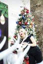 Beautiful blonde in a black dress hugs the figure of a deer near the Christmas tree Royalty Free Stock Photo