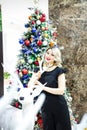 Beautiful blonde in a black dress hugs the figure of a deer near the Christmas tree Royalty Free Stock Photo